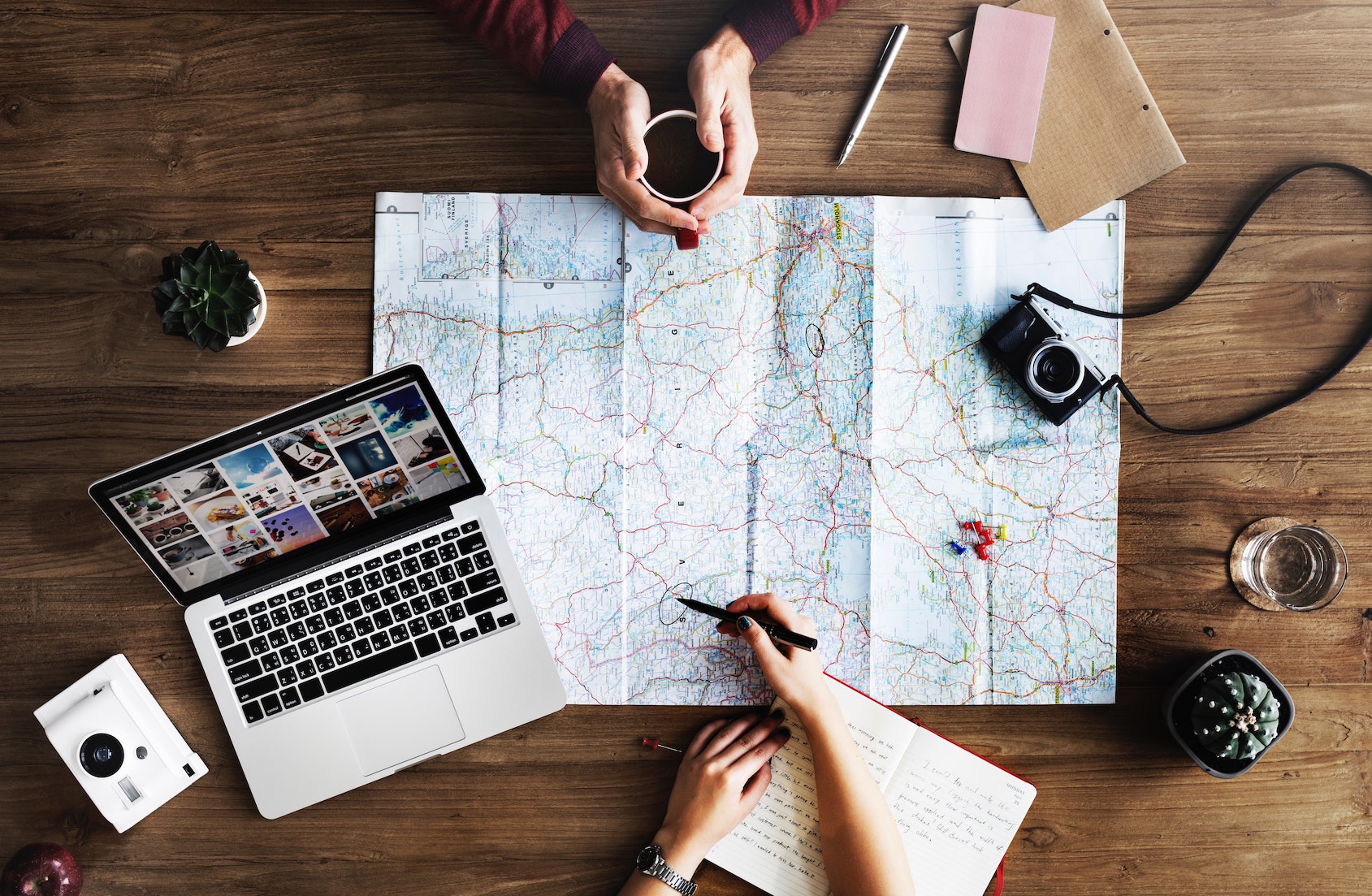 A map, camera and laptop on a wooden table.
